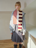 Model wearing a gray zip-up hoodie, a gray pleated skirt, and a striped scarf with pink, brown, and cream colors.