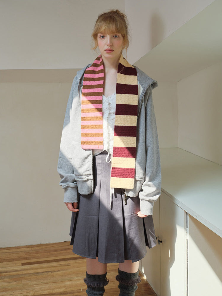 Model wearing a gray zip-up hoodie, a gray pleated skirt, and a striped scarf with pink, brown, and cream colors.