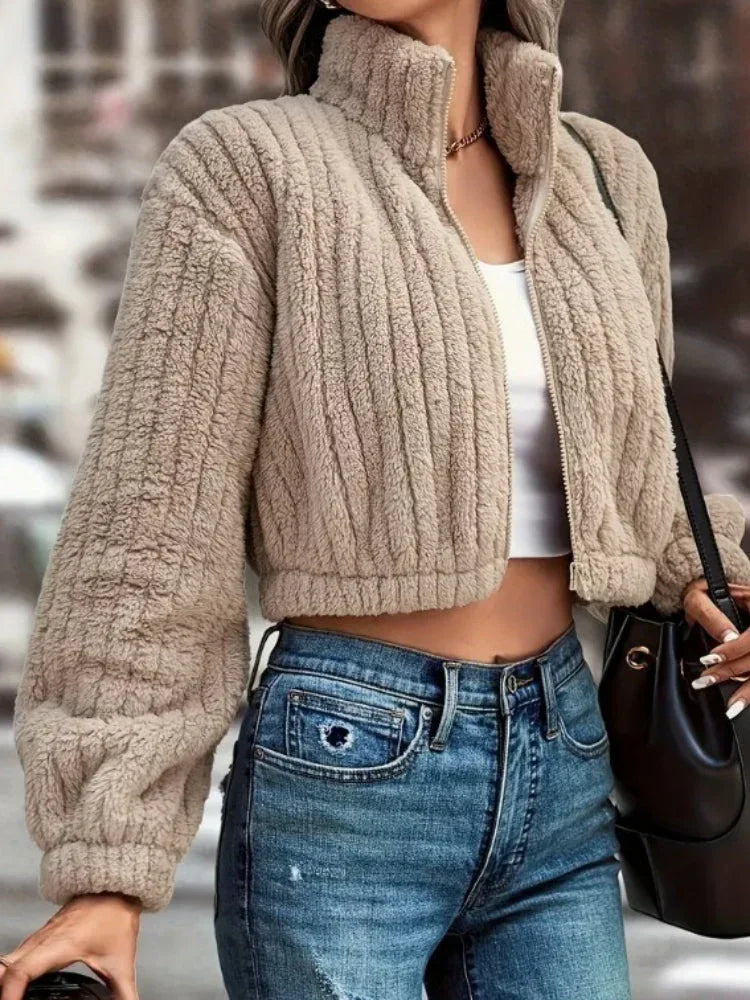 Close-up of a woman wearing a tan fuzzy fleece cropped bomber jacket over a white top.