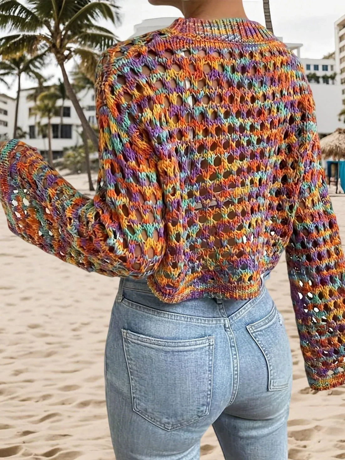 Woman wearing a multi-color cropped hollow-out knit sweater with bell sleeves and light wash jeans