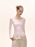 Front view of a model showcasing a light pink long-sleeve top with a square neckline.