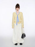 Woman posing with hands in pockets wearing a yellow cardigan and white pants