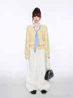 Woman posing with hands in pockets wearing a yellow cardigan and white pants