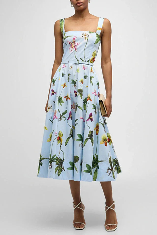 Woman wearing a light blue midi dress with a bold floral print, wide shoulder straps, and a belted waist. Main image