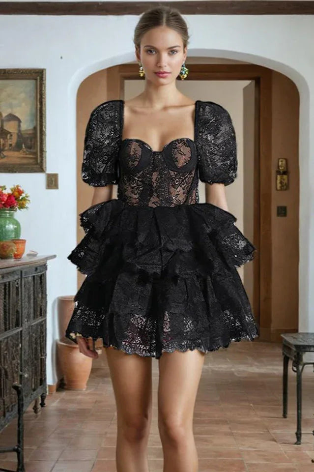 Woman wearing a black lace mini dress with puffed sleeves and a tiered skirt.