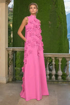 Woman in a pink column dress with floral appliqués and a mock neck, standing on a balcony.