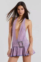 Woman wearing a lavender washed denim halter neck mini dress with a plunging V-neckline, a wide embellished belt, and a pleated skirt.