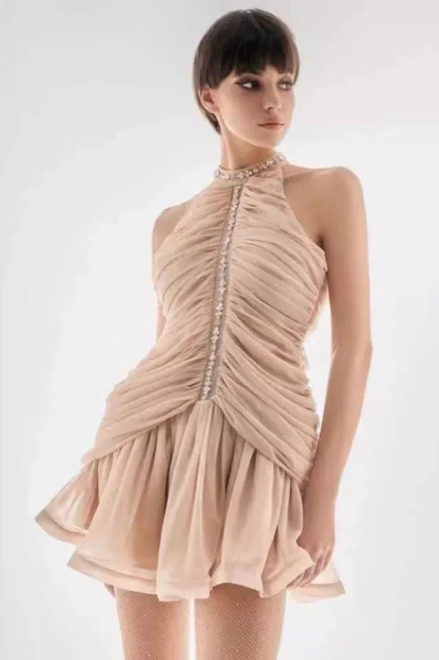 Woman wearing a ruched halter neck mini dress with embellished neckline in a light beige color.