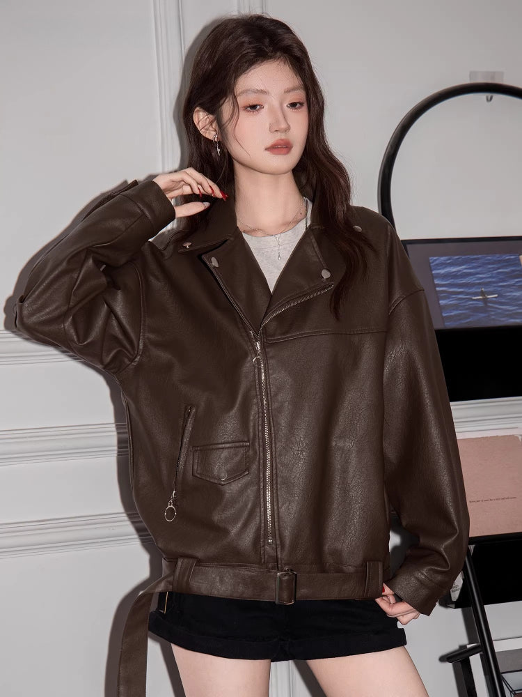 Woman wearing a brown faux leather moto jacket with a grey t-shirt and black shorts.
