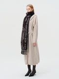 Side profile of a woman with blonde hair wearing a beige cardigan and a black scarf with text