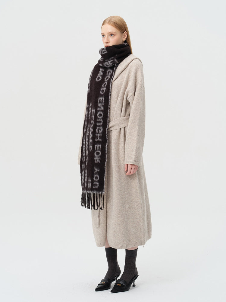 Side profile of a woman with blonde hair wearing a beige cardigan and a black scarf with text