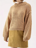 Woman wearing a tan chunky knit sweater with balloon sleeves and a mock neckline, paired with a mustard yellow skirt.