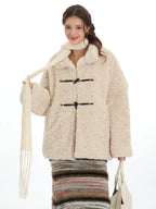 Woman wearing a cream fleece toggle coat and white scarf, holding a white tote bag