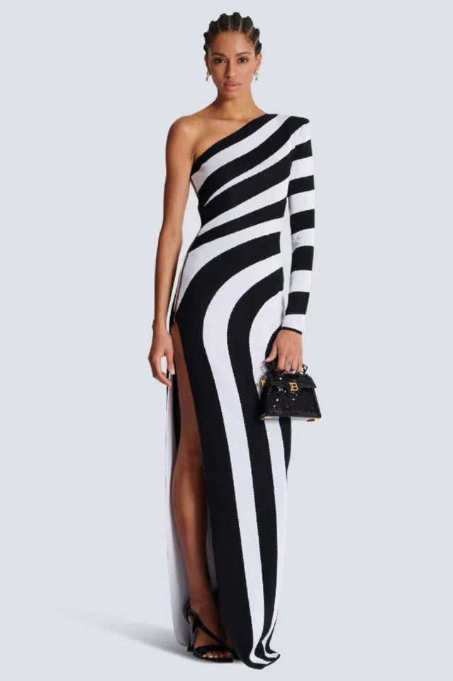 Woman wearing a black and white one-shoulder knit gown with a high slit and diagonal stripes