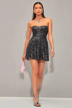 Full body shot of a woman in a black strapless sequin mini dress, holding a pink feather accessory.