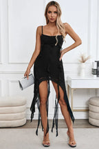Woman in a black chiffon spaghetti strap dress with a ruched bodice, ruffle trim, and an asymmetrical hemline with draped panels.