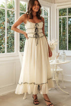 Woman posing in a cream spaghetti strap maxi dress with black contrast trim