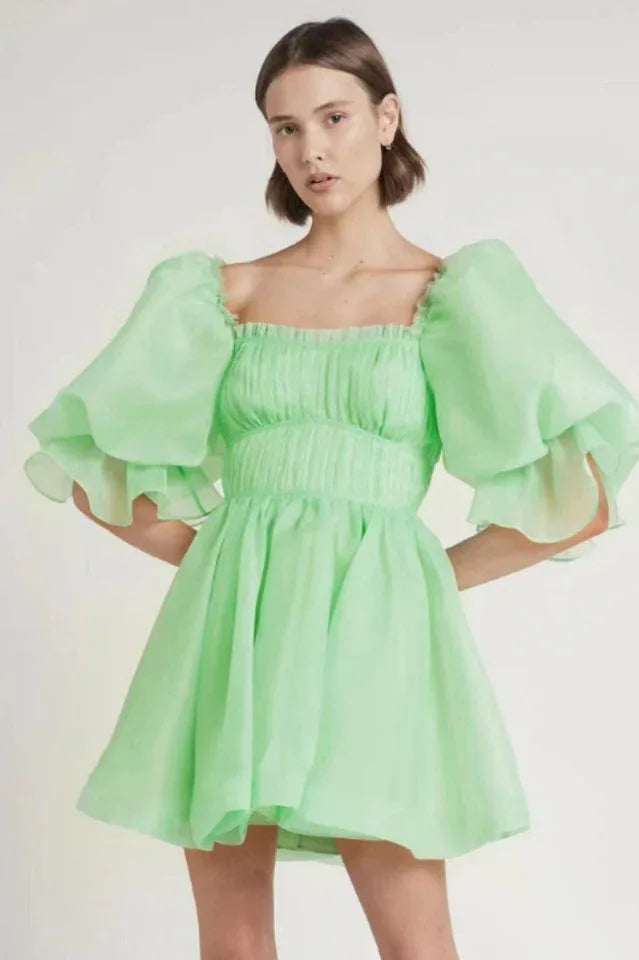 Woman wearing a light green organza mini dress with puffy sleeves and a square neckline Main image