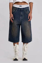 Front view of a model wearing medium wash denim culottes with a white cropped polo shirt and white lace-up boots.