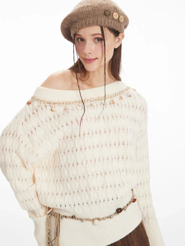 Detailed view of the neckline and upper chest area of a cream-colored off-the-shoulder knit sweater featuring a diamond pattern and decorative trim with small embellishments.