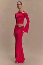 Woman wearing a red long-sleeved cropped top and a floor-length red skirt with a floral embellishment on the shoulder and hip.