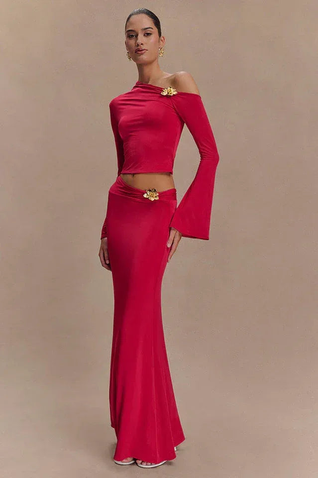 Woman wearing a red long-sleeved cropped top and a floor-length red skirt with a floral embellishment on the shoulder and hip.