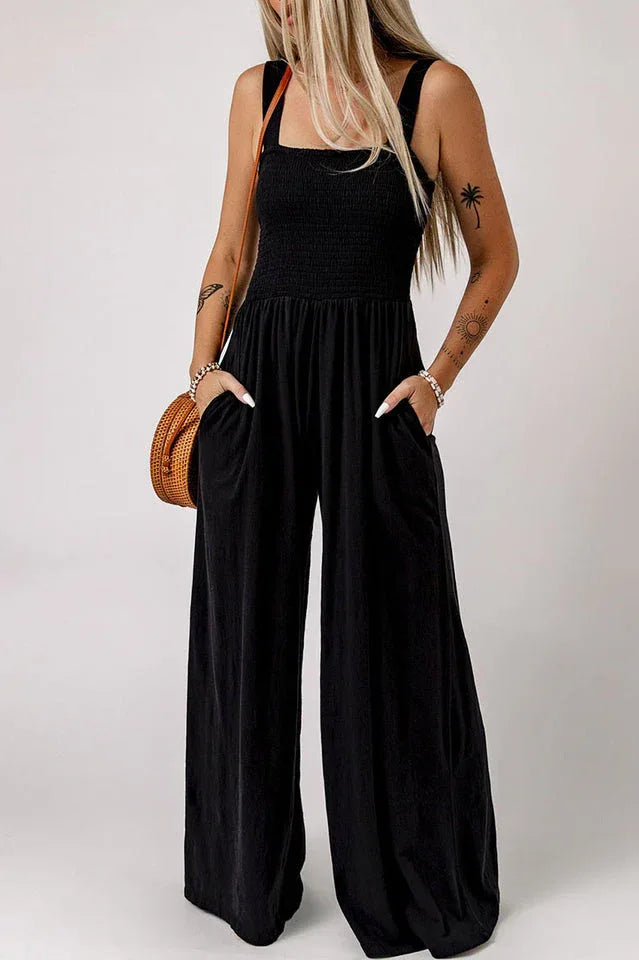 Woman wearing a black wide leg jumpsuit with a smocked bodice and square neckline