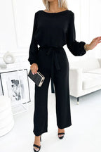 Model posing in a black long sleeve wide leg jumpsuit with a tie waist.