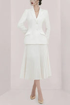Woman wearing a white tailored blazer and a white pleated midi skirt.