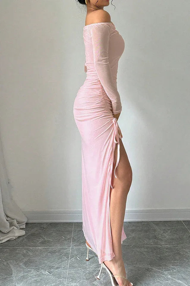 Side profile of a woman in a pink one-shoulder ruched maxi dress with a high leg slit.