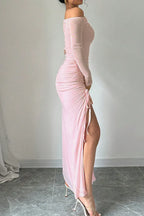 Side profile of a woman in a pink one-shoulder ruched maxi dress with a high leg slit.