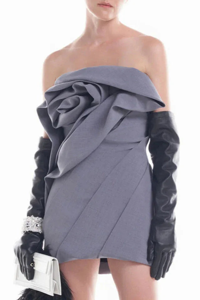 Woman wearing a grey strapless mini dress with a large floral embellishment on the bust, long black gloves, and a white clutch. Main image