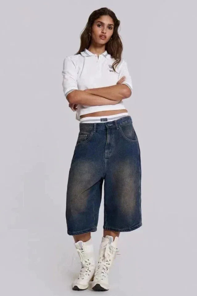 Woman wearing dark wash wide leg cropped denim culottes with a white cropped polo shirt and white lace-up boots.