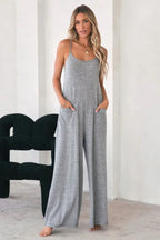 Woman in a grey jersey knit wide leg jumpsuit with patch pockets and spaghetti straps, standing.