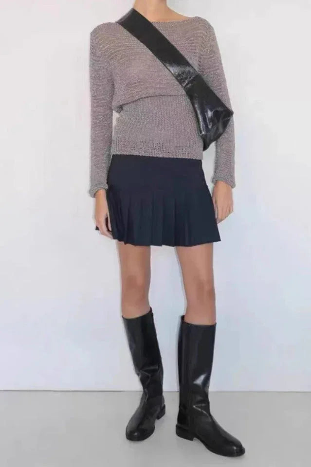 Model wearing a gray long-sleeve sweater, black pleated mini skirt, and black knee-high boots, accessorized with a black crossbody bag.