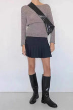 Model wearing a gray long-sleeve sweater, black pleated mini skirt, and black knee-high boots, accessorized with a black crossbody bag.