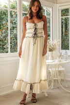 Woman wearing a cream maxi dress with black trim and lace-up detail