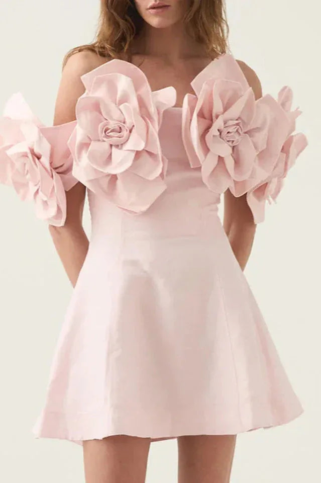 Woman wearing a light pink off-the-shoulder dress with large floral embellishments on the sleeves and a short A-line skirt. Main image