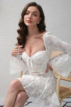 Woman sitting in a chair wearing a white lace mini dress with a sweetheart neckline.