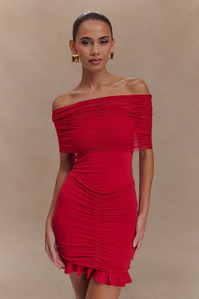 Woman wearing a red off-the-shoulder ruched mini dress with a sheer overlay and ruffled hem. Main image