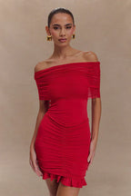 Woman wearing a red off-the-shoulder ruched mini dress with a sheer overlay and ruffled hem.