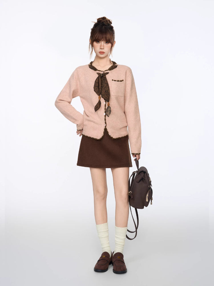 Woman wearing a light pink knit cardigan with dark brown trim and a decorative scarf