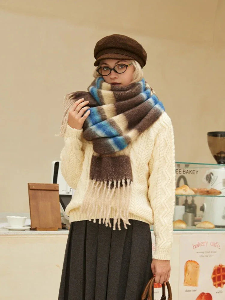 Woman wearing a cream cable knit sweater, dark gray skirt, and a brown plaid scarf with beige, brown, and blue stripes.