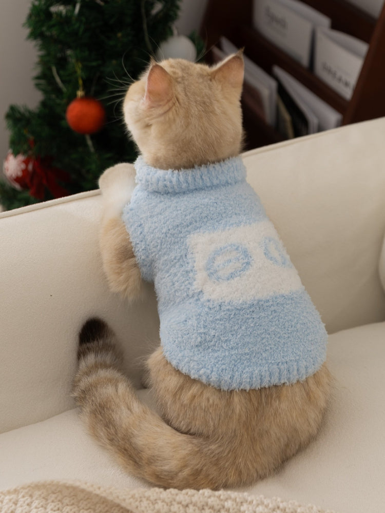 A light blue fluffy knit pet vest with a mock neck and a white logo patch on the front, worn by a light-colored cat.