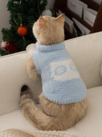 Rear view of a cat wearing a light blue fluffy knit pet vest with a mock neck and a white graphic detail on the back.
