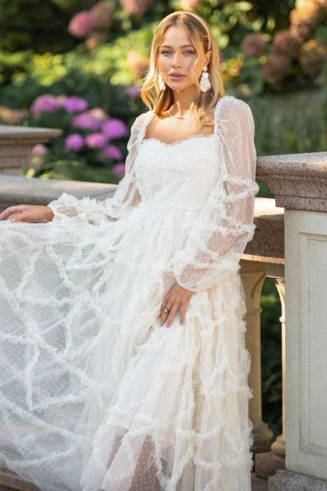 Woman in a white tiered ruffle tulle dress with sheer polka dot sleeves standing outdoors Main image