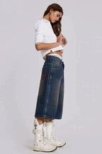 Side view of a model wearing medium wash denim culottes with a white cropped polo shirt and white lace-up boots.