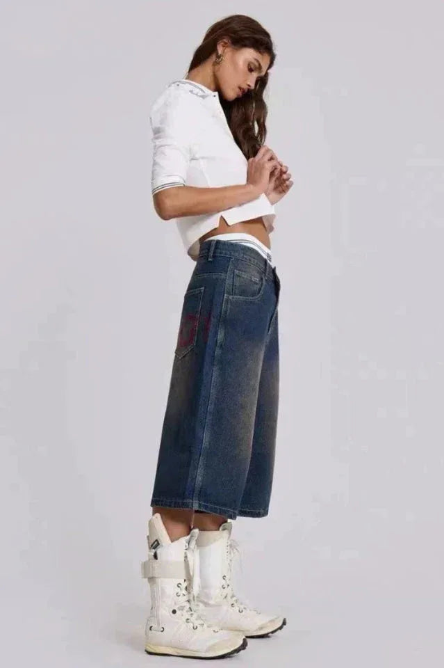Side view of a model wearing medium wash denim culottes with a white cropped polo shirt and white lace-up boots.