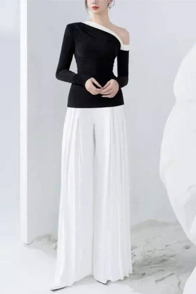 Full-length view of a woman in a black top with an asymmetrical neckline and white wide-leg pleated pants.