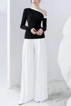 Full-length view of a woman in a black top with an asymmetrical neckline and white wide-leg pleated pants.